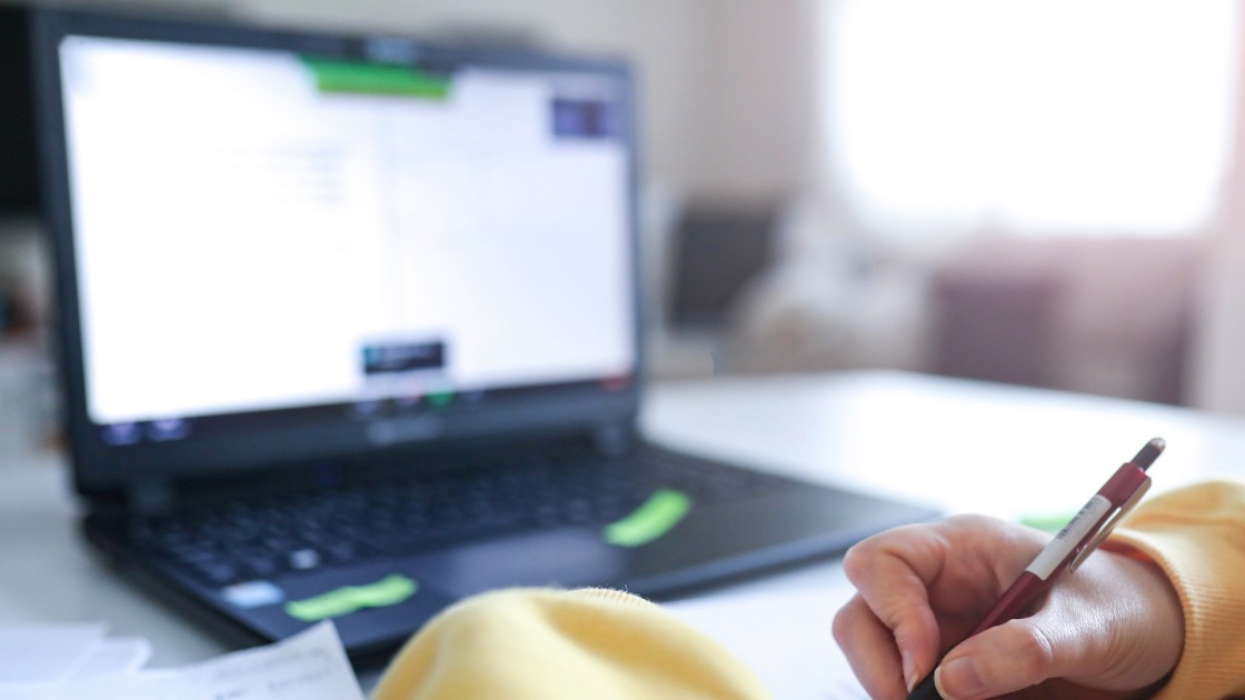 Student writing notes beside a laptop while following a step-by-step process to translate SAT word problems into equations.
